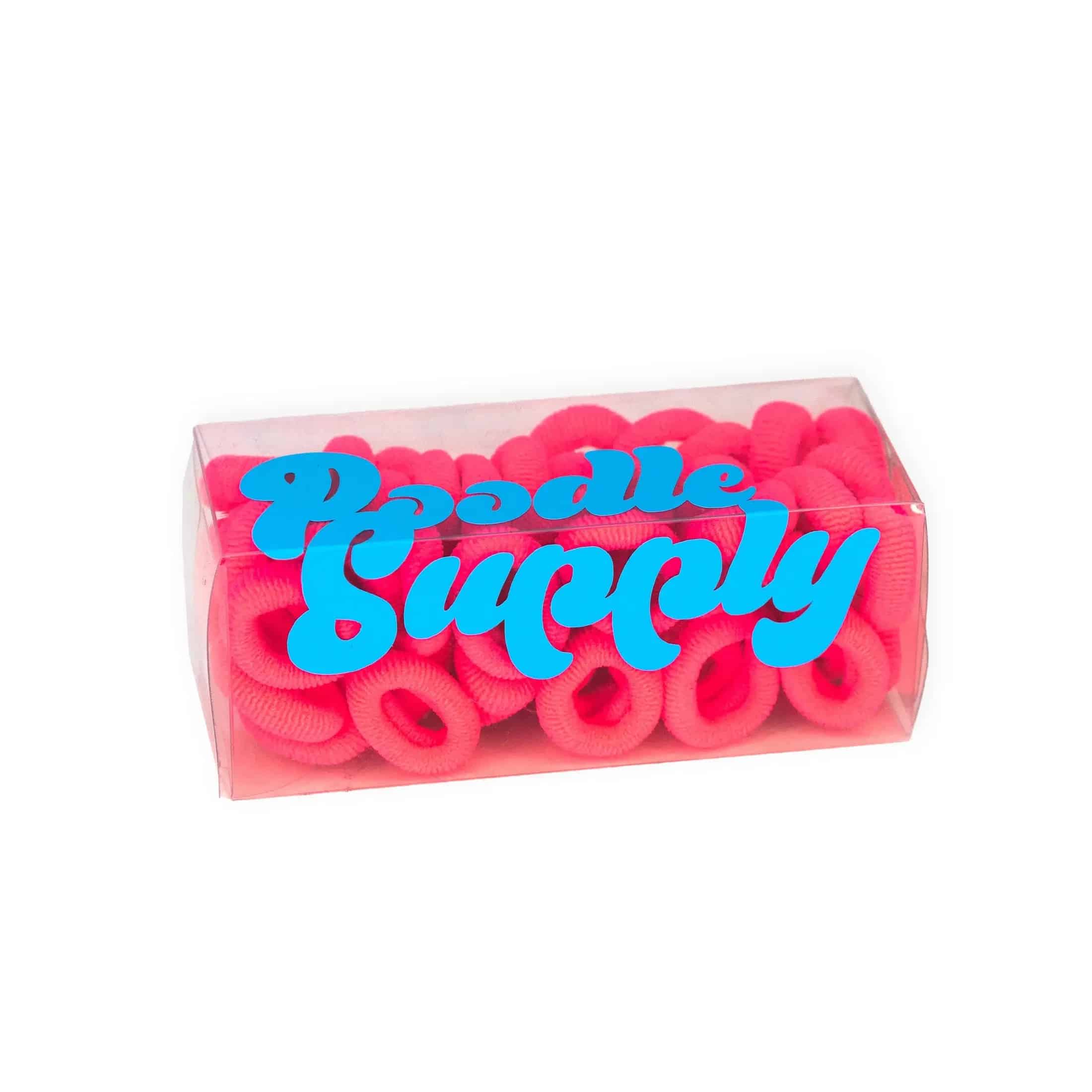 valkoinen tausta, pinkkejä froteelenksuja läpinäkyvässä rasiassa, tarrateksti missä lukee vaaleansinisellä poodle supply