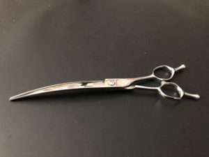 Koiran trimmaamiseen tarkoitetut kiiltävät hopean väriset kaarevat trimmaussakset mustalla pöydällä